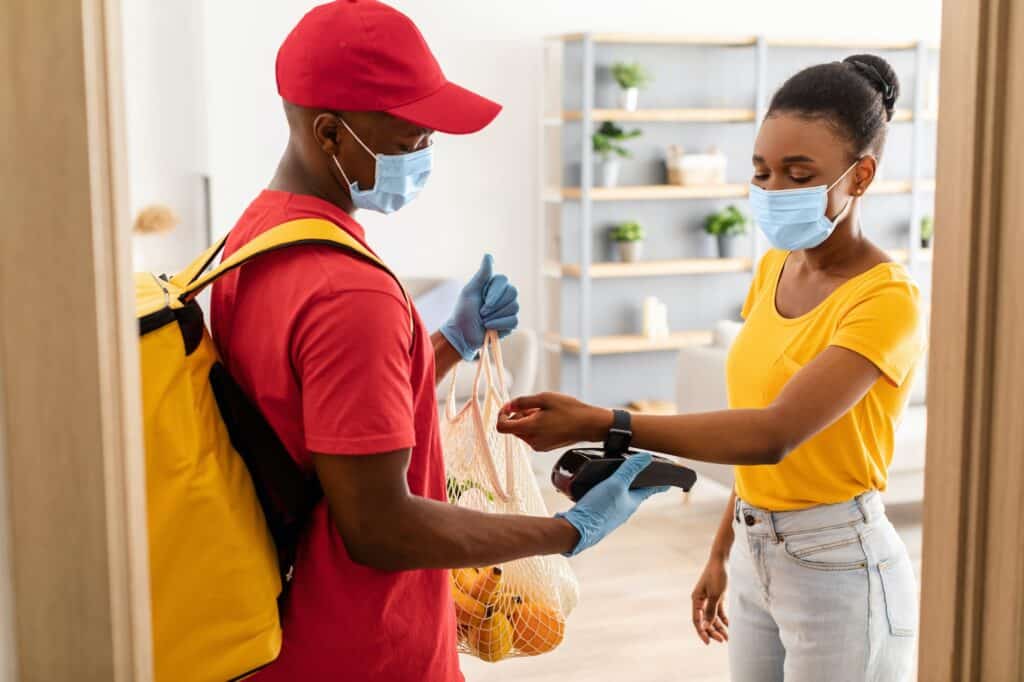 African Woman Paying Courier For Groceries With Smartwatch At Home